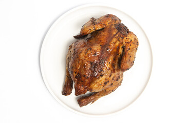 A whole delicious roasted chicken seasoned with herbs in a white plate top view isolated on white background clipping path