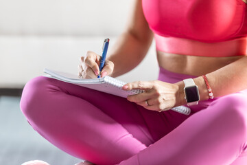 Sporty woman sits on a mat and writes down future training plans for achieving sports results - 748627110
