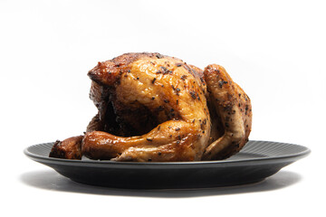 A whole delicious roasted chicken seasoned with herbs in a black plate isolated on white background clipping path