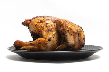 A whole delicious roasted chicken seasoned with herbs in a black plate isolated on white background clipping path