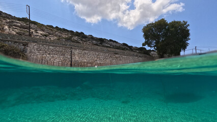 Underwater split photo of paradise crystal clear sea beach of Agios Georgios in main port of Irakleia island covered in Armirikia trees providing natural shade, small Cyclades, Greece