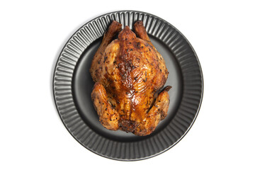 A whole delicious roasted chicken seasoned with herbs in a black plate top view isolated on white background clipping path