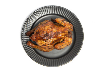 A whole delicious roasted chicken seasoned with herbs in a black plate top view isolated on white background clipping path