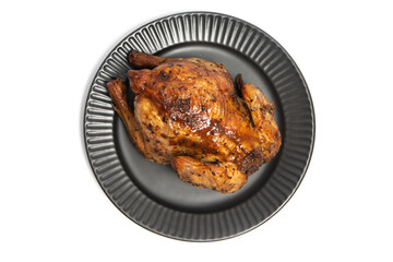 A whole delicious roasted chicken seasoned with herbs in a black plate top view isolated on white background clipping path