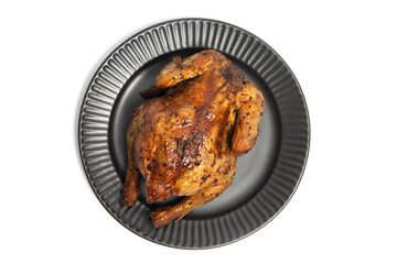 A whole delicious roasted chicken seasoned with herbs in a black plate top view isolated on white background clipping path