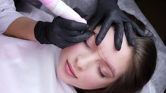 Beautiful brunette on permanent eyebrow makeup procedure. Permanent makeup procedure, performing PMU of eyebrows