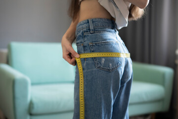 Young Woman in blue jeans Measuring Her Hips With a Yellow Tape Measure at home