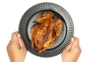 Hand holding a whole delicious roasted chicken seasoned with herbs in a black plate top view isolated on white background clipping path