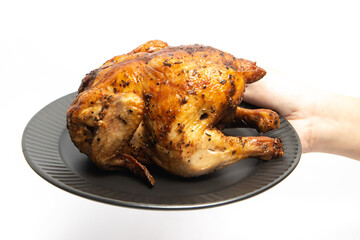Hand holding a whole delicious roasted chicken seasoned with herbs in a black plate isolated on white background clipping path