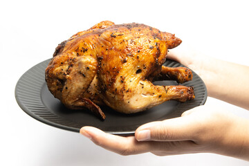 Hand holding a whole delicious roasted chicken seasoned with herbs in a black plate isolated on white background clipping path