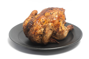 A whole delicious roasted chicken seasoned with herbs in a black plate isolated on white background clipping path