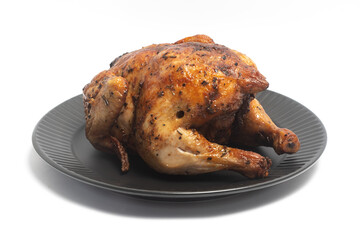 A whole delicious roasted chicken seasoned with herbs in a black plate isolated on white background clipping path