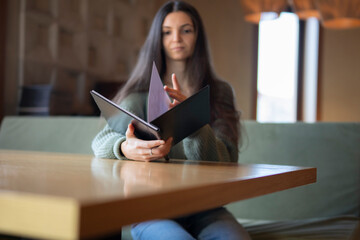 Young Woman Seated on a Green Sofa Choosing a Meal From a Menu in cafe