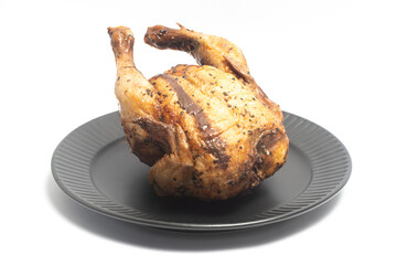 A whole delicious roasted chicken seasoned with herbs in a black plate isolated on white background clipping path