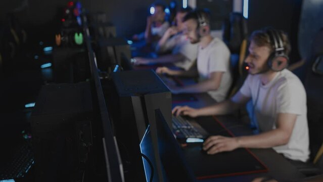 Team of gamers playing video game on PC at cyber club during E-sport championship, focus on computers. Five players in headset are at sport tournament. Multiplayer online strategy RTS tactical shooter