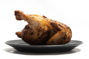 A whole delicious roasted chicken seasoned with herbs in a black plate isolated on white background clipping path
