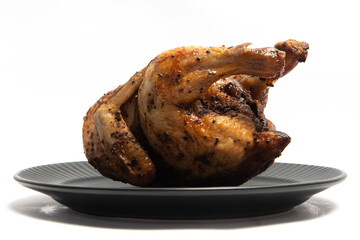 A whole delicious roasted chicken seasoned with herbs in a black plate isolated on white background clipping path