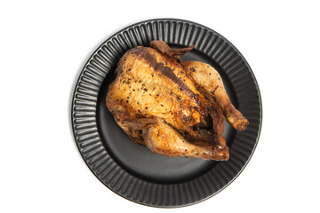 A whole delicious roasted chicken seasoned with herbs in a black plate top view isolated on white background clipping path