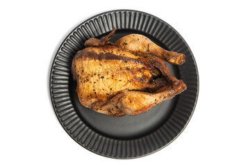 A whole delicious roasted chicken seasoned with herbs in a black plate top view isolated on white background clipping path