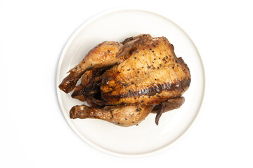 A whole delicious roasted chicken seasoned with herbs in a white plate top view isolated on white background clipping path