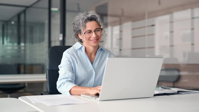 Happy middle aged professional business woman working in office using computer laptop looking away. Smiling older lady executive corporate leader at workplace thinking of new business ideas.