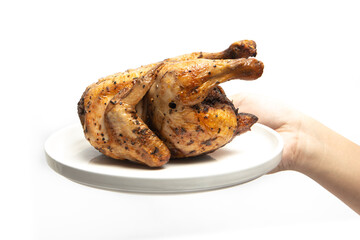 Hand holding a whole delicious roasted chicken seasoned with herbs in a white plate isolated on white background clipping path