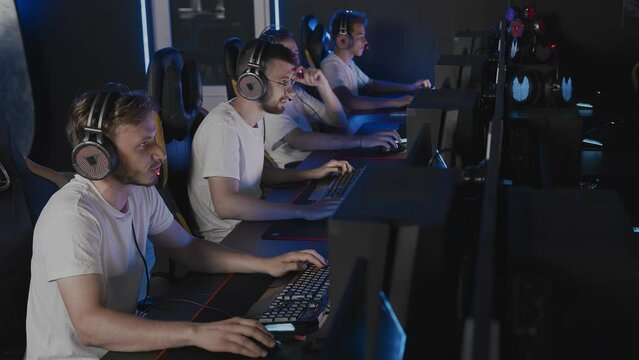 Gamers team playing video game on PC at cyber club during E-sport championship, rack focus from computers to players in headset, sport tournament. Multiplayer online strategy RTS tactical shooter