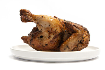 A whole delicious roasted chicken seasoned with herbs in a white plate isolated on white background clipping path