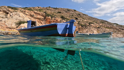 Underwater split photo of traditional fishing boat anchored in crystal clear sea of Mykonos island,...