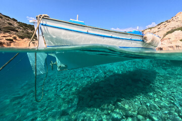Underwater split photo of traditional wooden fishing boat anchored in turquoise sea of rocky bay in...