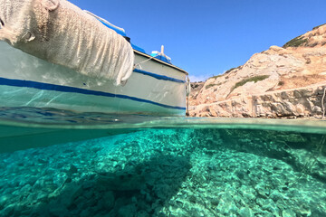 Underwater split photo of traditional wooden fishing boat anchored in turquoise sea of rocky bay in...