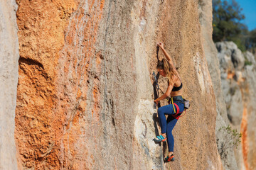 The girl climbs the rock. The climber is training to climb the rock. A strong athlete overcomes a difficult climbing route. Extreme hobby. .