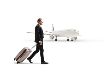 Full length profile shot of a businessman walking and pulling a suitcase near an airplane
