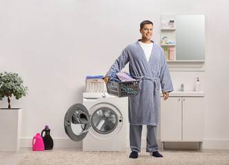 Young man in a bathrobe holding a laundry basket in a bathroom - Powered by Adobe