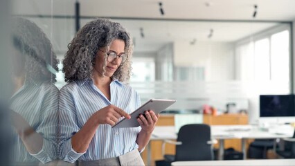 Middle aged professional business woman using tab computer in office. Mature busy happy businesswoman bank manager, older female corporate executive holding digital tablet standing at work. - Powered by Adobe