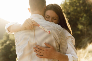 a couple with a pregnancy test hugs while outdoors. happy family concept. husband and wife are expecting a child. pregnancy test
