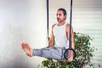 Concentrated adult man doing L Sit calisthenic exercise with rings at home