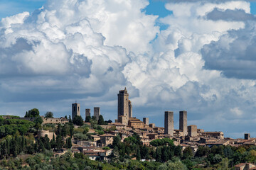 Skyline view of walled medieval hill town San Gimignano in Tuscany, Italy known as the Town of Fine Towers famous for its medieval architecture of tower houses with dramatic clouded sky - obrazy, fototapety, plakaty