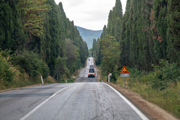 View over part of the 5 km tree-lined road with several cars Viale dei Cipressi (Boulevard of Cypresses) near Bolgheri, Italy which connects San Guide with historic centre of the village of Bolgher - obrazy, fototapety, plakaty