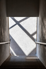 High angle view down the exit of a sparsely lit concrete stairwell with handrails on both side...