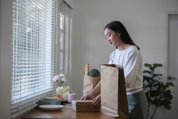 A beautiful young woman unwraps a paper bag with vegetables and fruits and prepares to make a healthy meal in the kitchen.