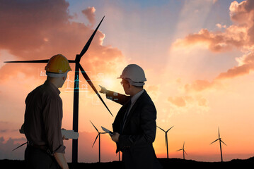 Two engineers with blueprints discussing wind turbines during a vibrant sunset in the background..