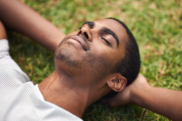 Face, relax and black man on grass in garden of summer home for peace, wellness or mindfulness. Nature, field and sunshine with happy young person lying on green ground from above for break or rest