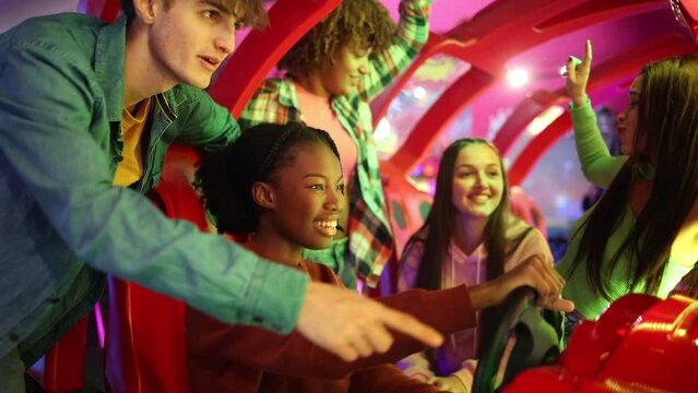 young african american woman driving with steering wheel arcade game in arcade with her multiracial friends celebrating and dancing