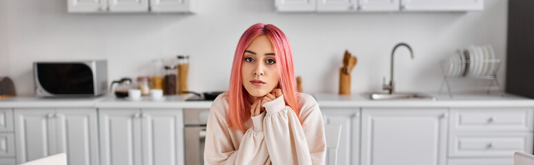 appealing young pink haired woman in comfy homewear looking at camera while in kitchen at home