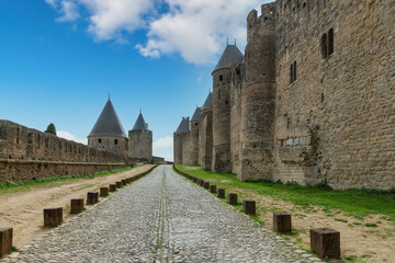 Fototapeta na wymiar View over length of moat between rows of fortified walls with battlement and towers of Carcassonne, France, a medieval fortress from Gallo-Roman period and part of UNESCO list of World Heritage Sites