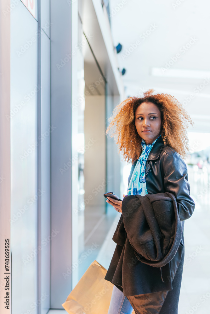 Canvas Prints Young black girl looks at her mobile phone in front of the window of a store inside a shopping center