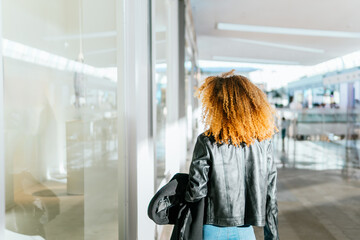 Young black girl with afro hair walks through the shops of a shopping center window shopping. She...
