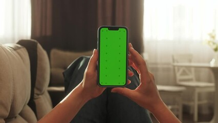 Close up of unrecognizable woman at cozy living room using smartphone with green screen and scrolling.
