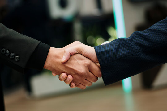 hombres de primer plano d&aacute;ndose la mano. Se puede ver un poco de su antebrazo, uno lleva un traje negro y el otro un traje azul oscuro.